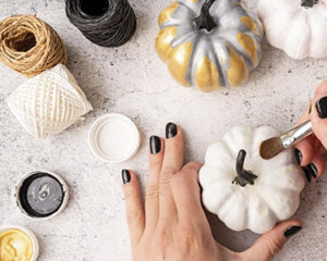 Halloween concept. Halloween DIY craft. Woman hands with a paintbrush coloring pumpkins for a holiday flat lay top view